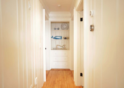 narrow hallway with white wooden walls, light brown wood floor, and showcase shelving on the back wall