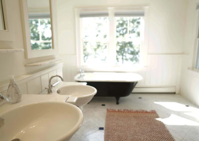 bathroom with two white sinks to the left and freestanding tub at the back with large window behind it