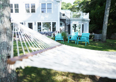 image of the side of a large White House with blue lawn chairs and white hammock in the forefront